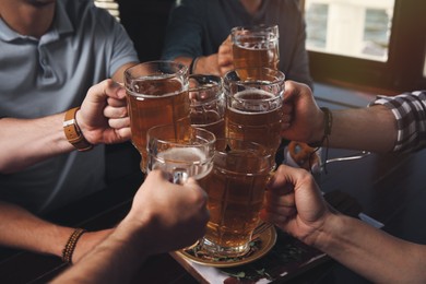 Photo of Friends clinking glasses with beer in pub, closeup