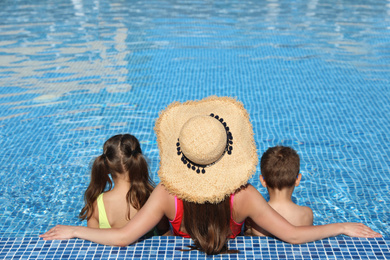Photo of Woman with her children in swimming pool, back view. Summer vacation