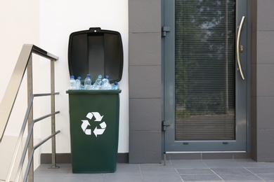 Many used plastic bottles in trash bin near entrance outdoors. Recycling problem