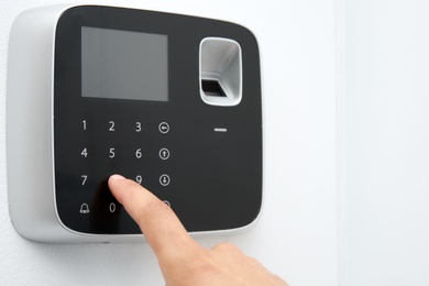 Young man entering code on alarm system keypad indoors