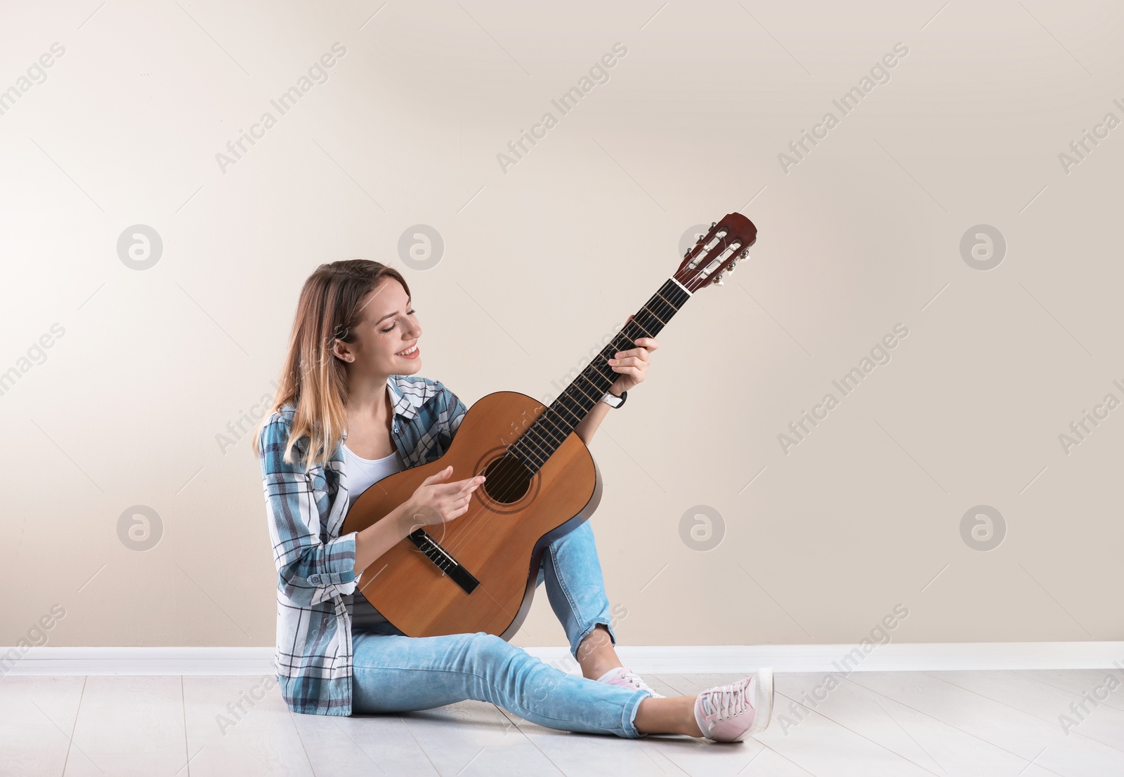 Photo of Young woman playing acoustic guitar near grey wall. Space for text