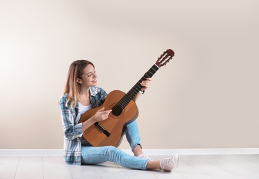 Photo of Young woman playing acoustic guitar near grey wall. Space for text