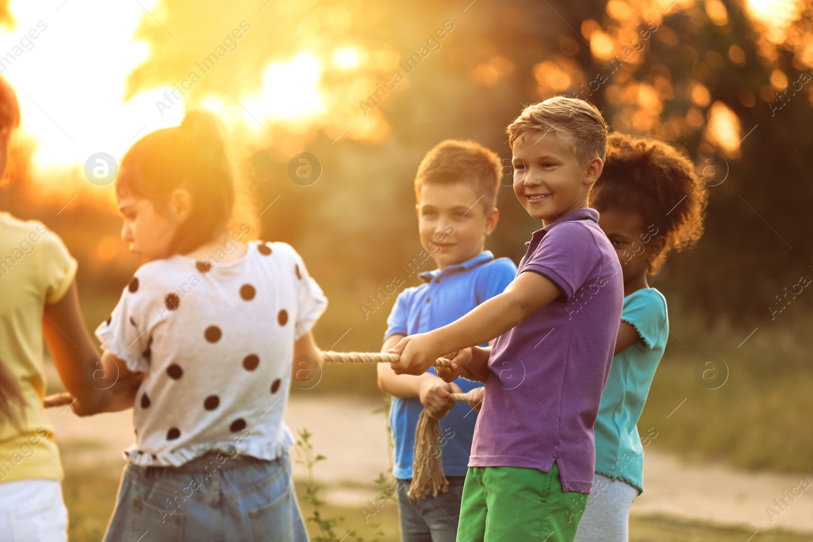 Image of Cute little children playing tug of war game in park at sunset