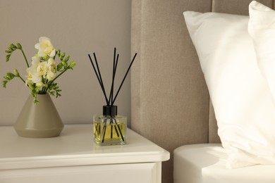 Photo of Aromatic reed air freshener and freesia flowers on white bedside table in bedroom