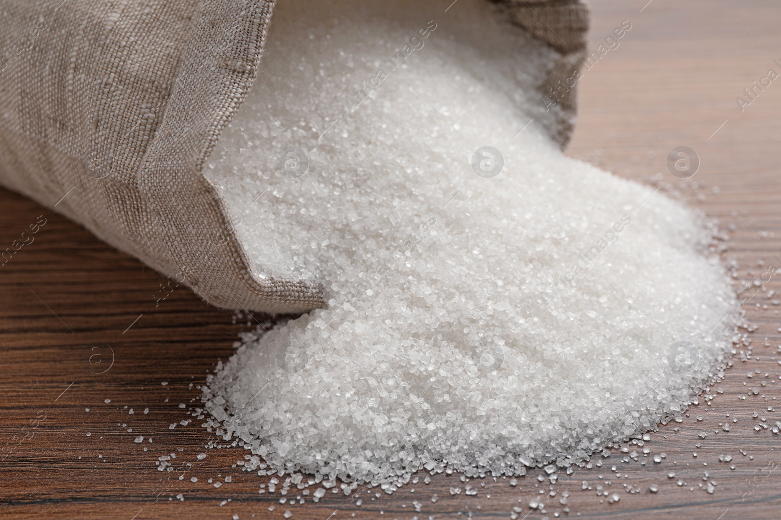 Photo of Overturned sack bag with granulated sugar on wooden table, closeup