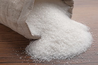 Overturned sack bag with granulated sugar on wooden table, closeup