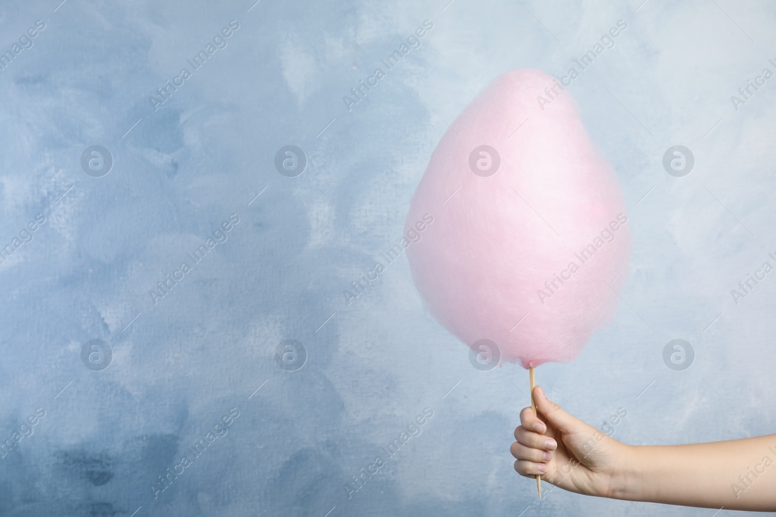 Photo of Woman holding sweet pink cotton candy on light blue background, closeup view. Space for text