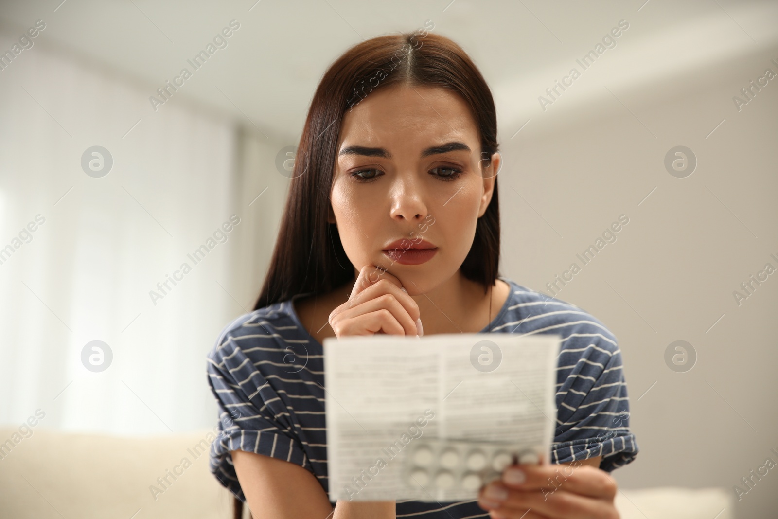 Photo of Confused young woman with pills reading medicine instruction indoors