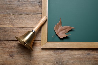Photo of Golden school bell and green chalkboard with autumn leaf on wooden table, flat lay