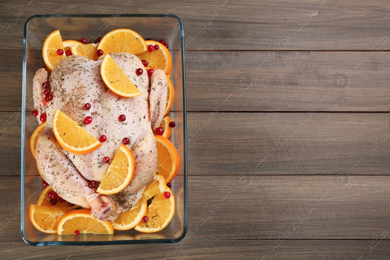Photo of Raw chicken with orange slices and cranberries on wooden table, top view. Space for text