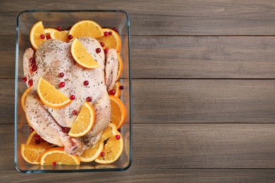 Photo of Raw chicken with orange slices and cranberries on wooden table, top view. Space for text