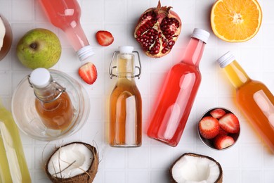 Tasty kombucha in glass bottles and fresh fruits on white tiled table, flat lay