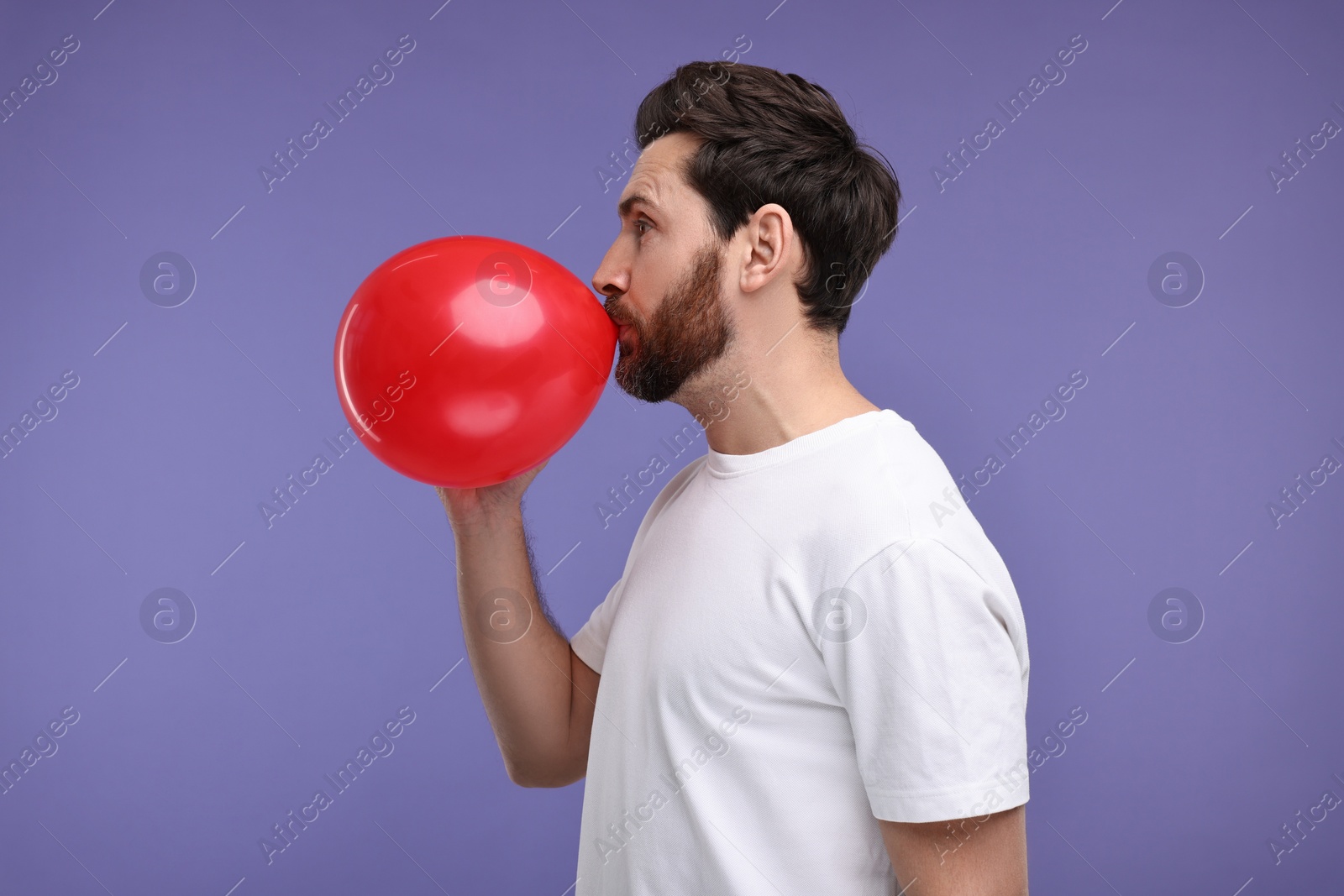 Photo of Man inflating red balloon on purple background