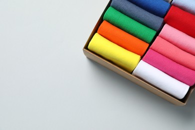 Box with different colorful socks on light background, top view. Space for text