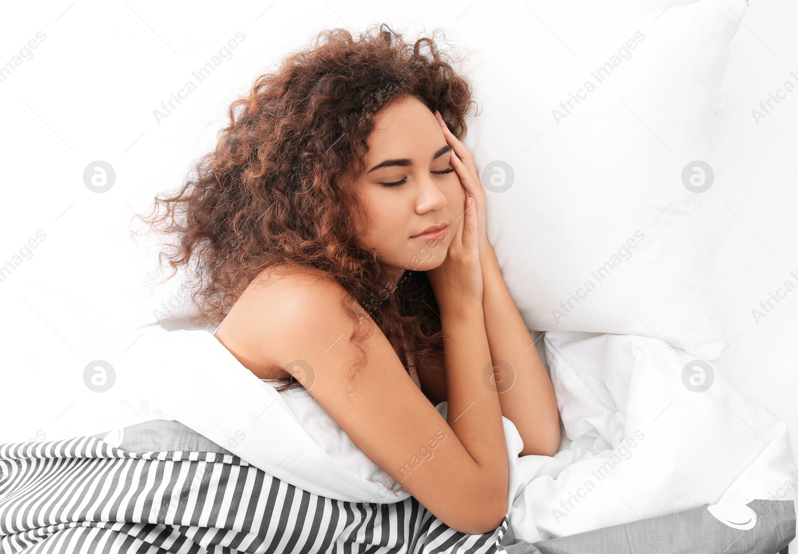 Photo of Young African-American woman sleeping on soft pillow, top view. Bedtime