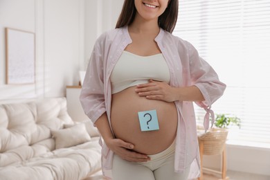 Photo of Pregnant woman with sticky note on belly at home, closeup. Choosing baby name