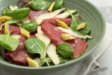 Photo of Delicious bresaola salad in bowl on light table, closeup