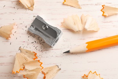 Pencil, sharpener and shavings on white wooden table, flat lay