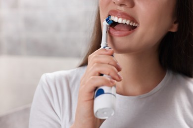 Photo of Woman brushing her teeth with electric toothbrush indoors, closeup