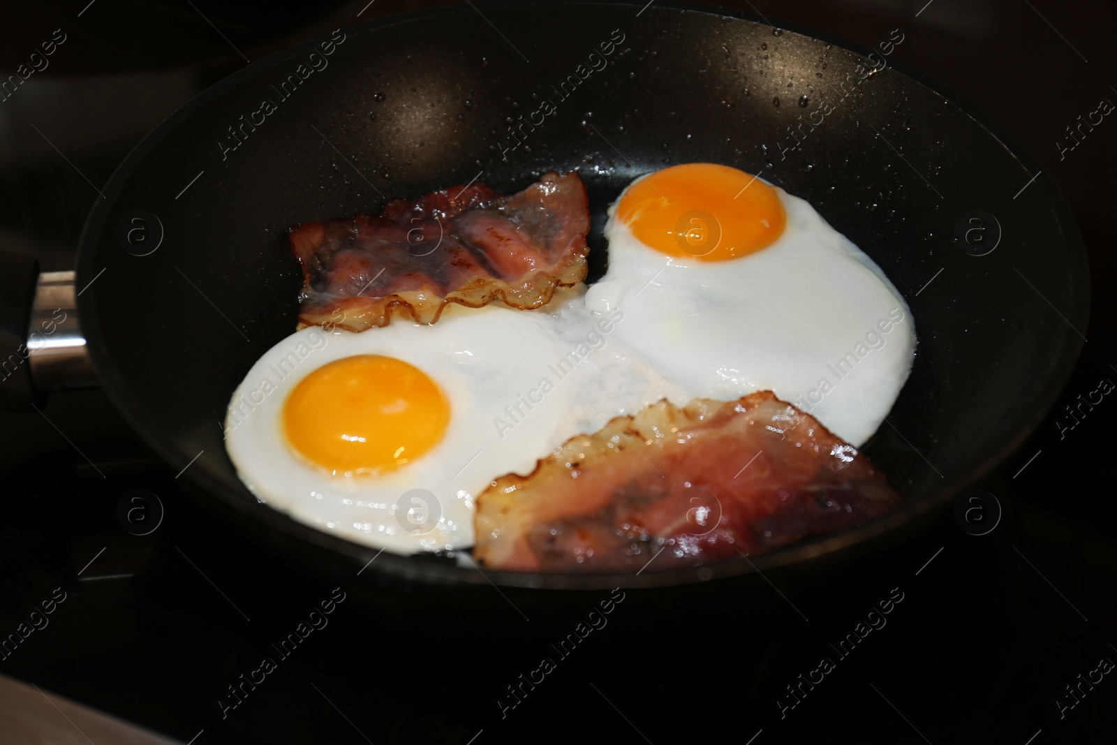 Photo of Cooking eggs with bacon in frying pan, closeup. Tasty breakfast