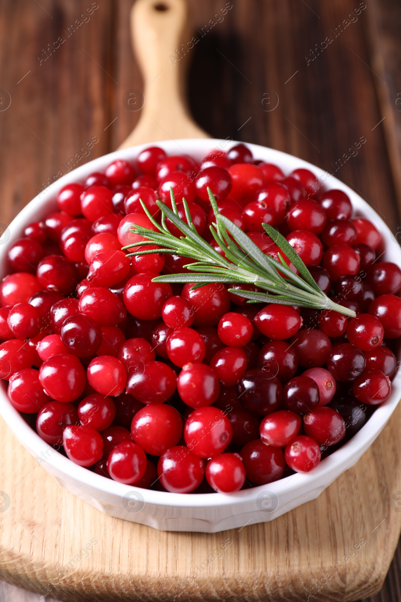 Photo of Fresh ripe cranberries and rosemary in bowl on wooden table, closeup