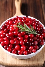 Fresh ripe cranberries and rosemary in bowl on wooden table, closeup