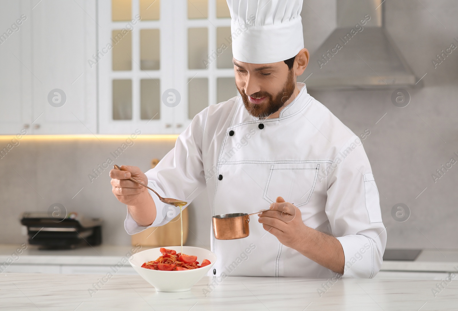 Photo of Professional chef pouring sauce into delicious spaghetti at marble table