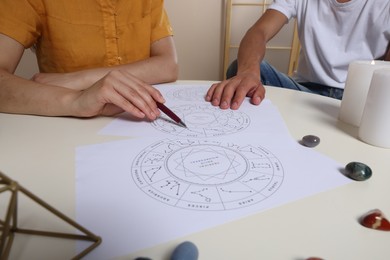 Photo of Astrologer showing natal charts to client at table indoors, closeup