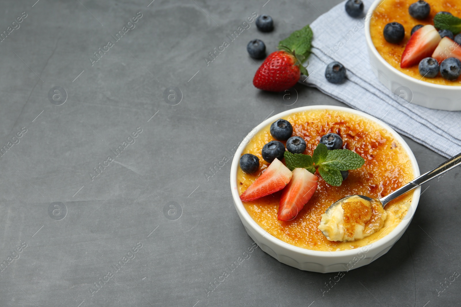 Photo of Delicious creme brulee with berries in bowl and spoon on grey table. Space for text