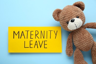 Photo of Toy bear and note with words Maternity Leave on light blue background, flat lay
