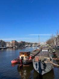 Amsterdam, Netherlands - March 01, 2023: Picturesque view of river embankment with moored boats in city under blue sky