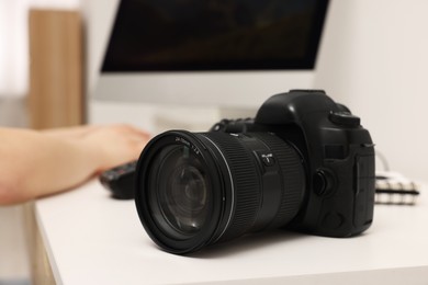 Photo of Photographer working on computer at white table with camera indoors, closeup