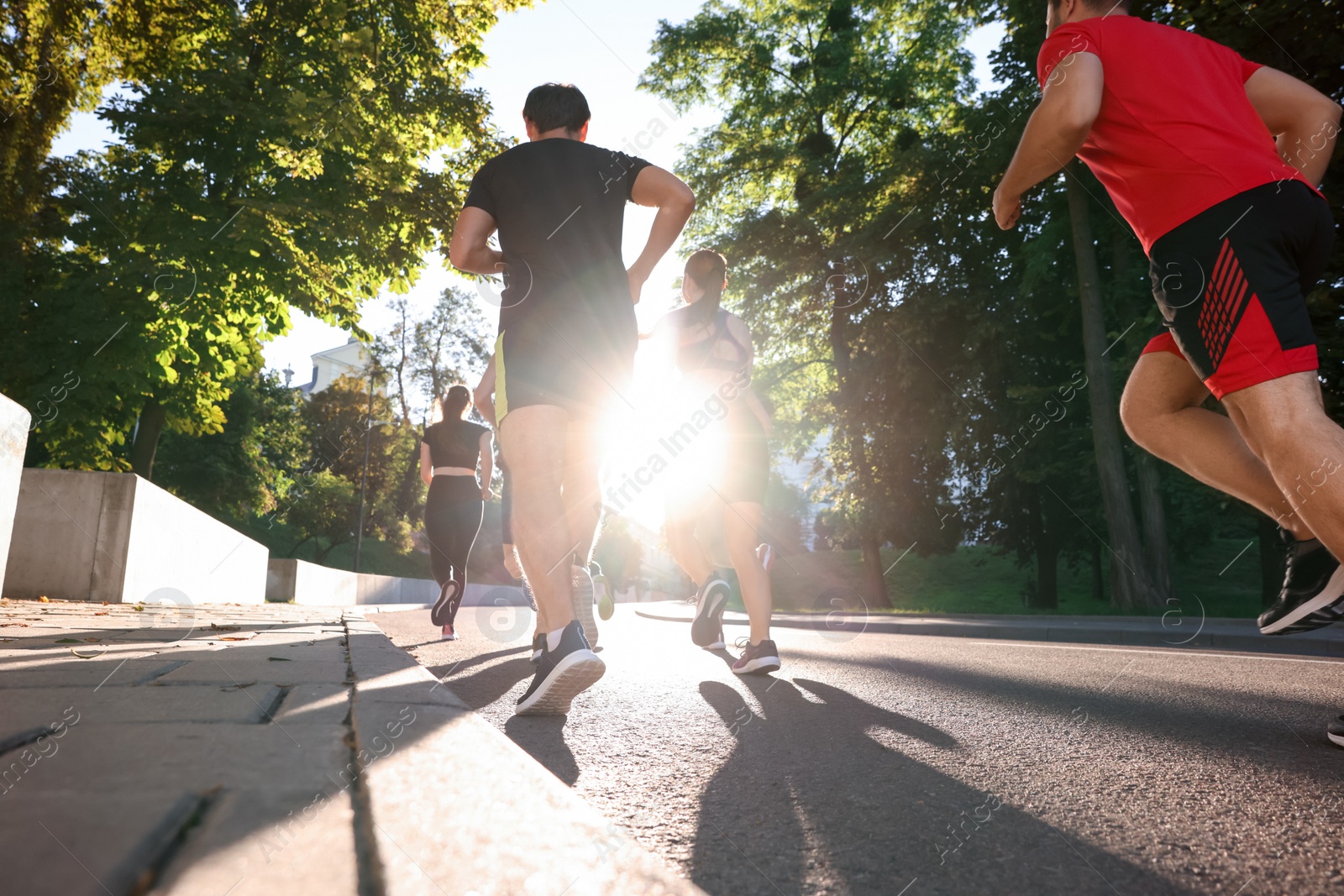 Photo of Group of people running outdoors on sunny day, back view