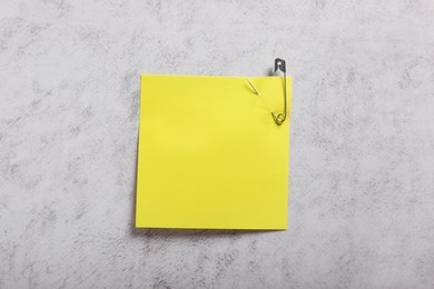 Photo of Yellow paper note with safety pin on grey textured background, top view