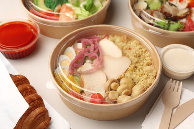 Photo of Tasty food in containers with wooden knife and fork on light grey table, closeup