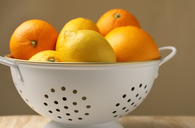 Photo of Colander with fresh citrus fruits on table, closeup