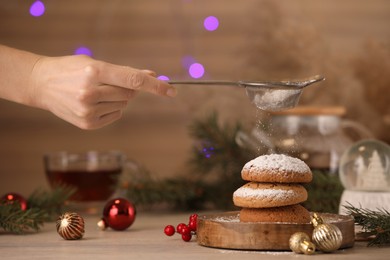 Photo of Woman sieving icing sugar on cookies at wooden table, closeup