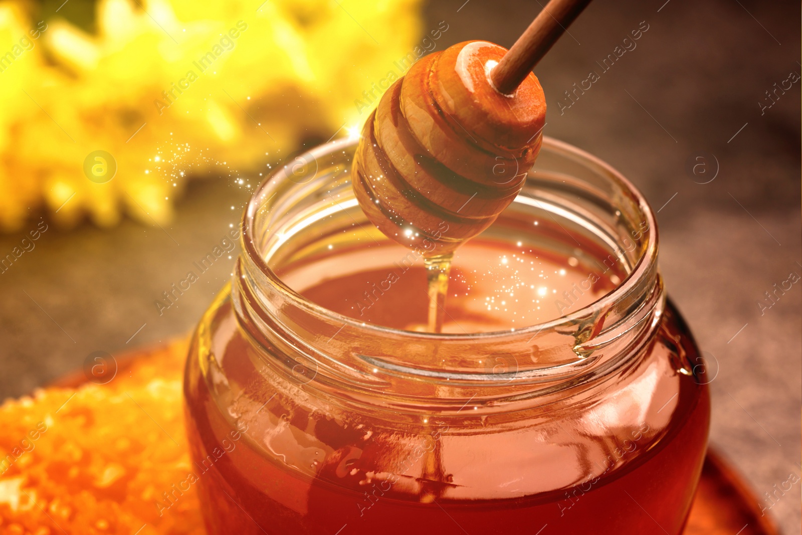 Image of Natural honey dripping from dipper into glass jar under sunlight, closeup