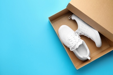 Photo of Stylish sport shoes in box on light blue background, top view. Space for text