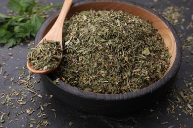 Photo of Plate and spoon with dried parsley on black table, closeup