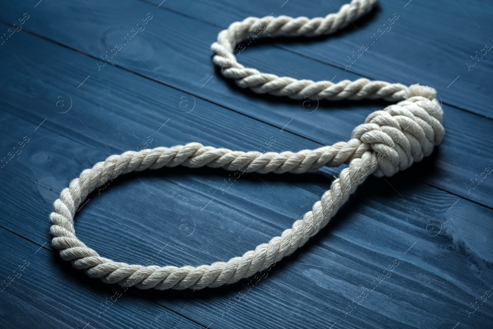 Photo of Rope noose with knot on blue wooden table, closeup