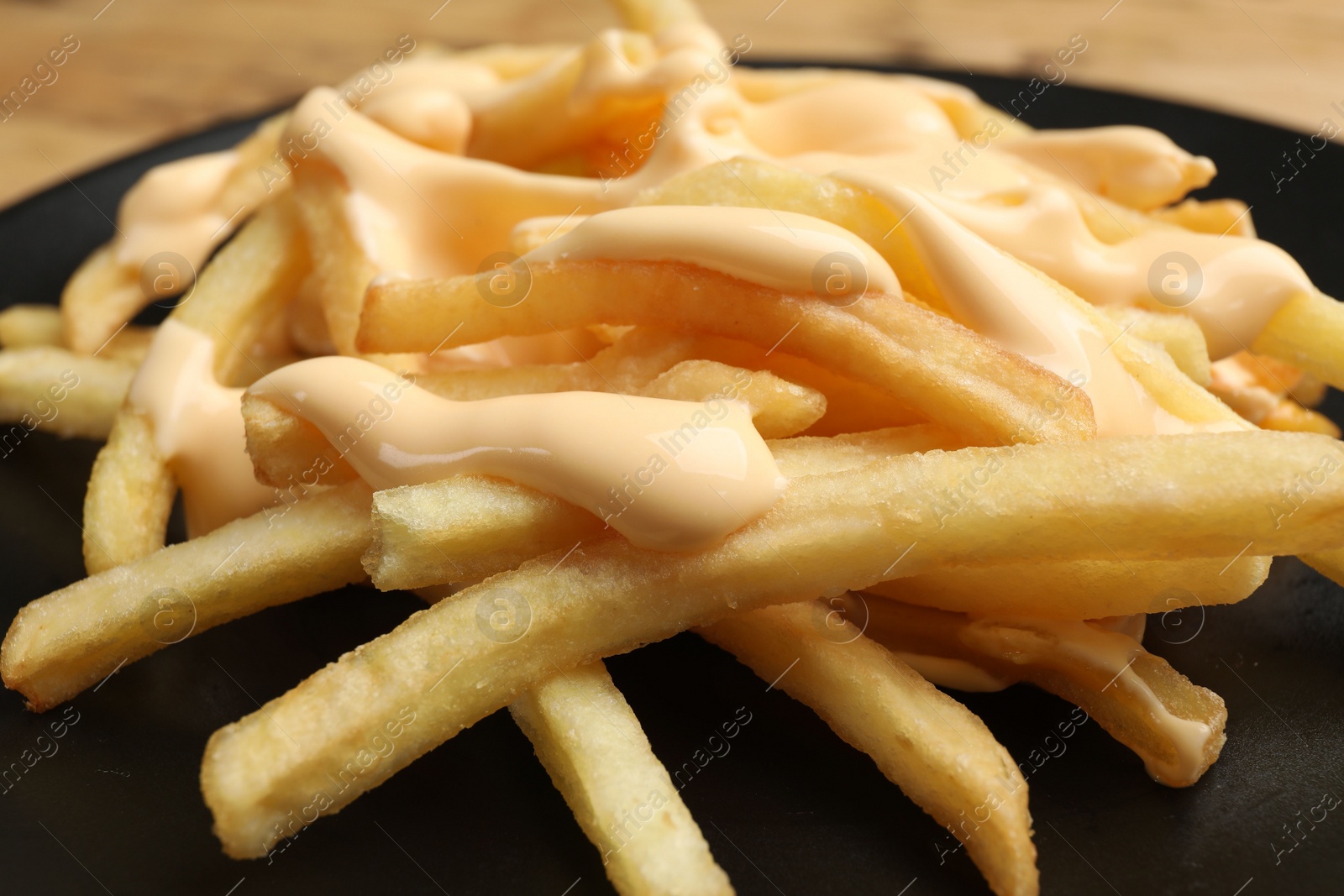 Photo of Delicious French fries with cheese sauce on plate, closeup