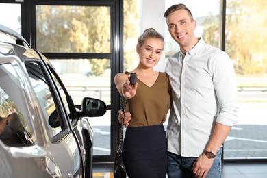 Photo of Young couple with key near new car in dealership