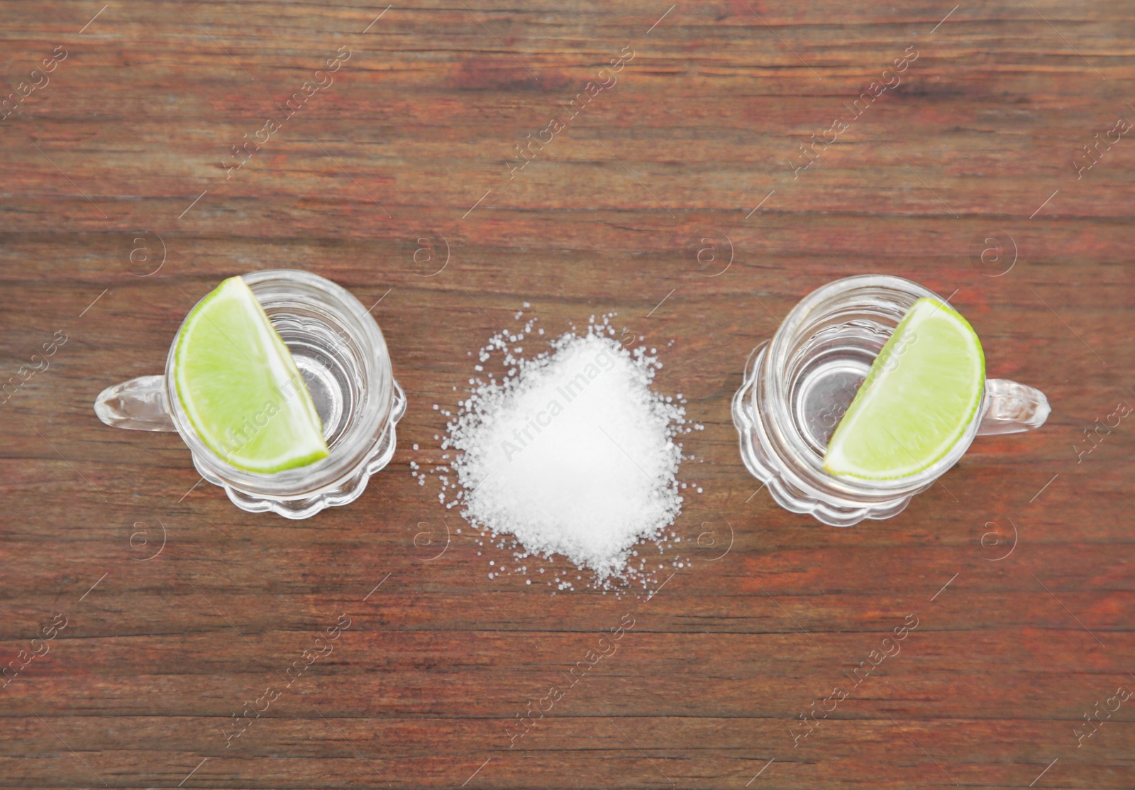 Photo of Mexican tequila shots with lime slices and salt on wooden table, flat lay. Drink made from agave