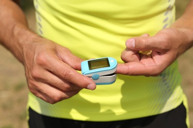 Photo of Young man checking pulse with medical device after training outdoors, closeup