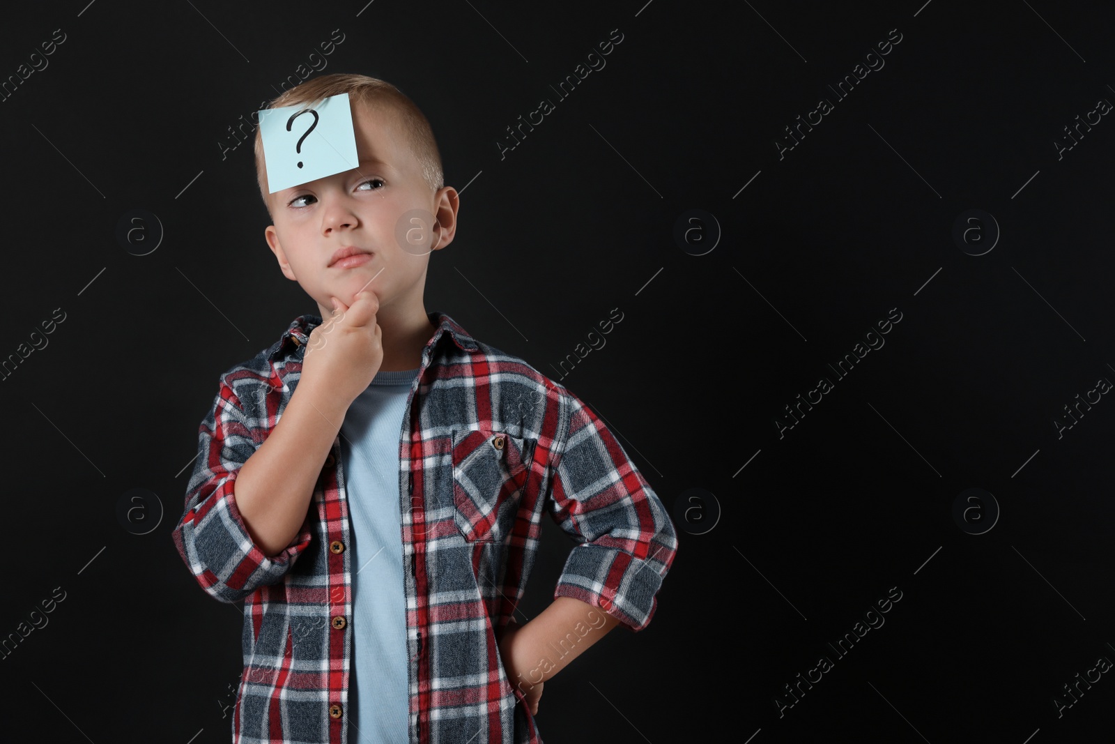 Photo of Pensive boy with question mark sticker on forehead against black background. Space for text