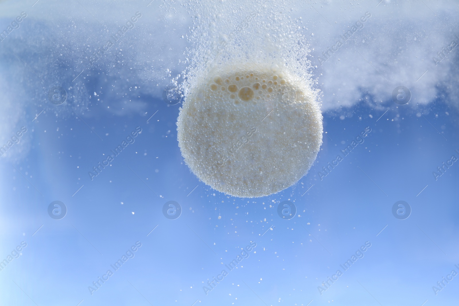 Photo of Effervescent pill dissolving in water on light blue background, closeup