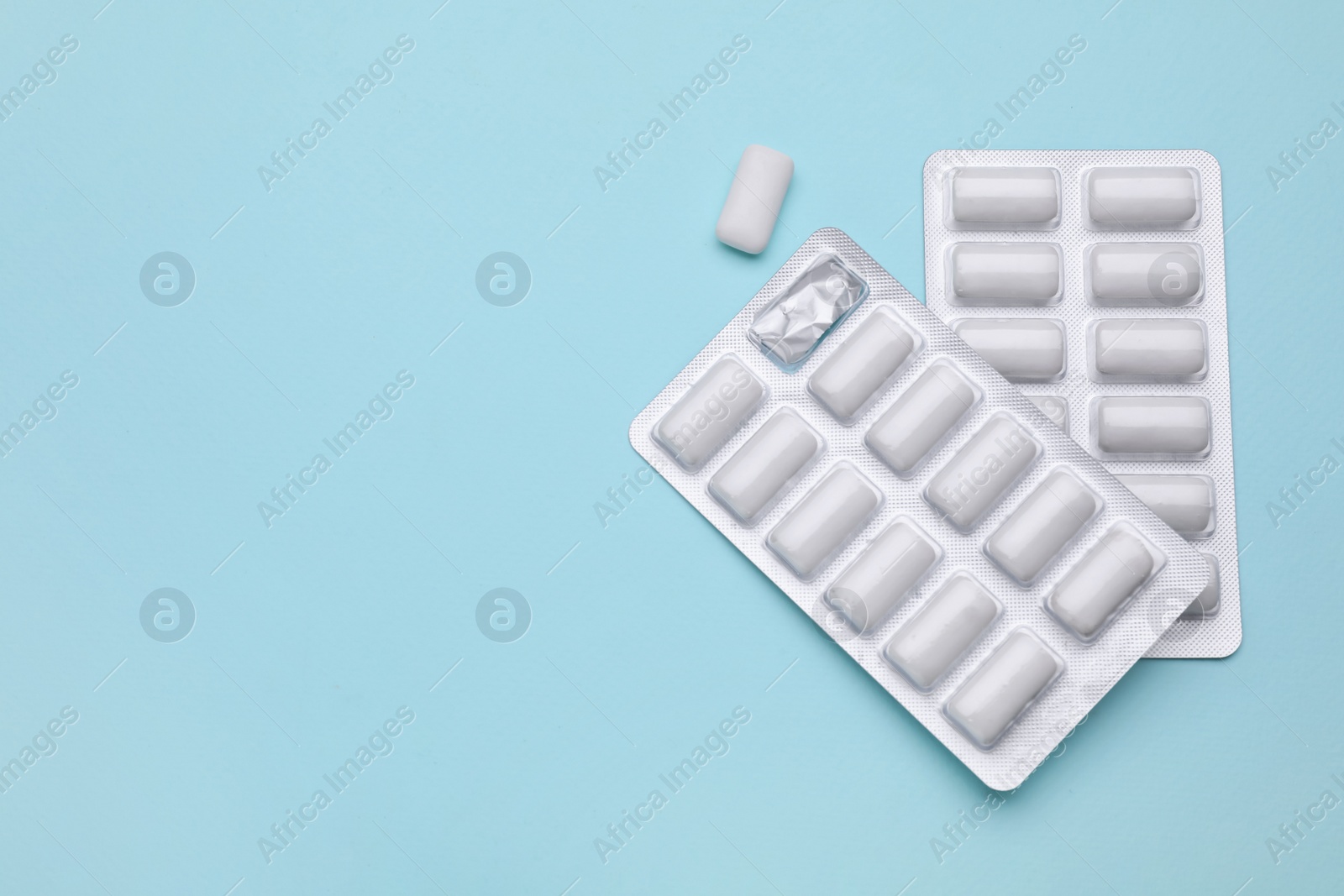 Photo of Blisters with chewing gums on light blue background, flat lay. Space for text