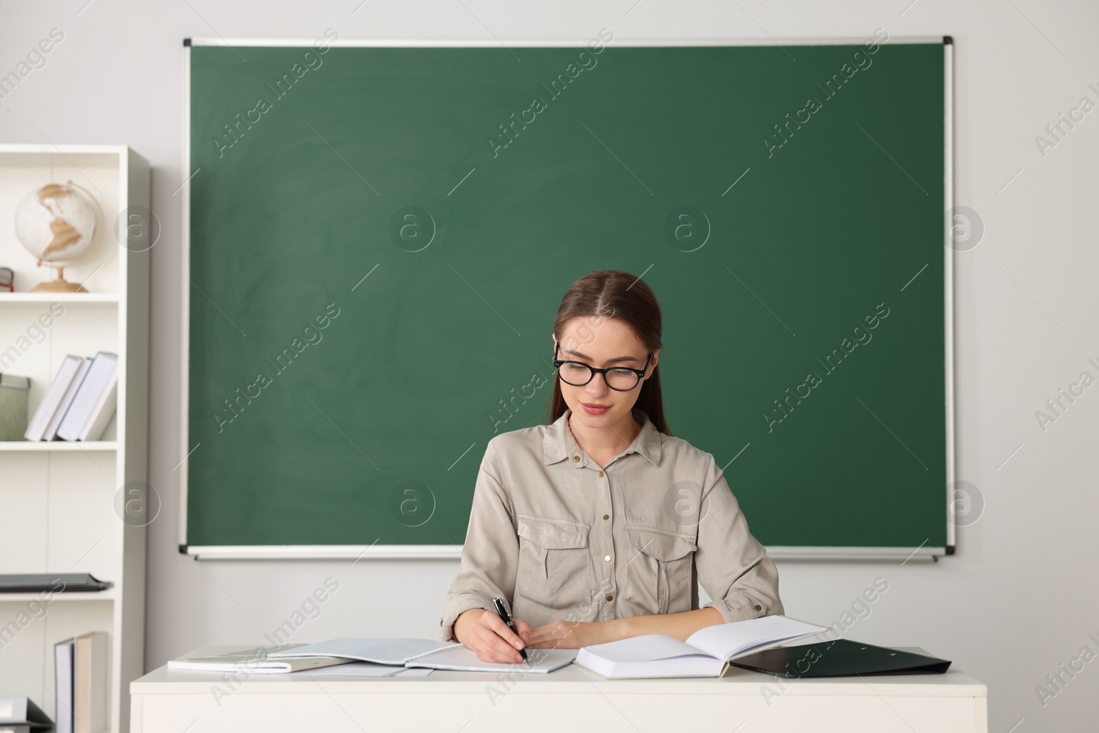 Photo of Beautiful young teacher giving lesson at table in classroom