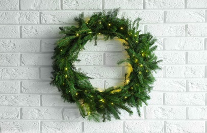 Photo of Beautiful Christmas wreath with festive lights on white brick wall